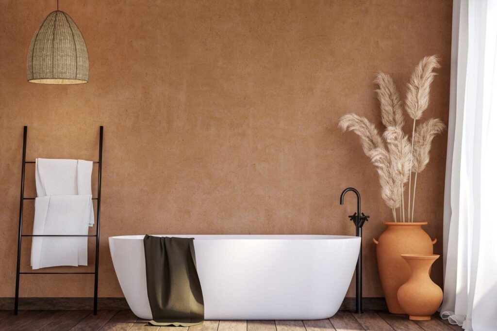 Minimalist bathroom with an earth-toned color palette. Backwall painted in a terracotta color, terracotta vases with dried flowers, large modern bathtub and white towels