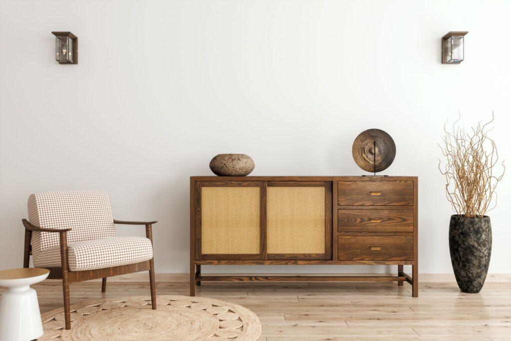 Modern African home design : a wooden armchair with whote cushions on a natural woven rug, a stunning wooden console table with a wooden bowl and a makenge basket on it. A large clay vase with a dried grass in it.