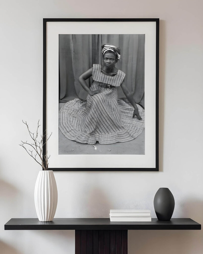A black and white photo by Seydou Keita, representing a woman in a patterned dress and headscarf, sits on a wall over a modern console table. The photo displays a sense of poise and elegance.