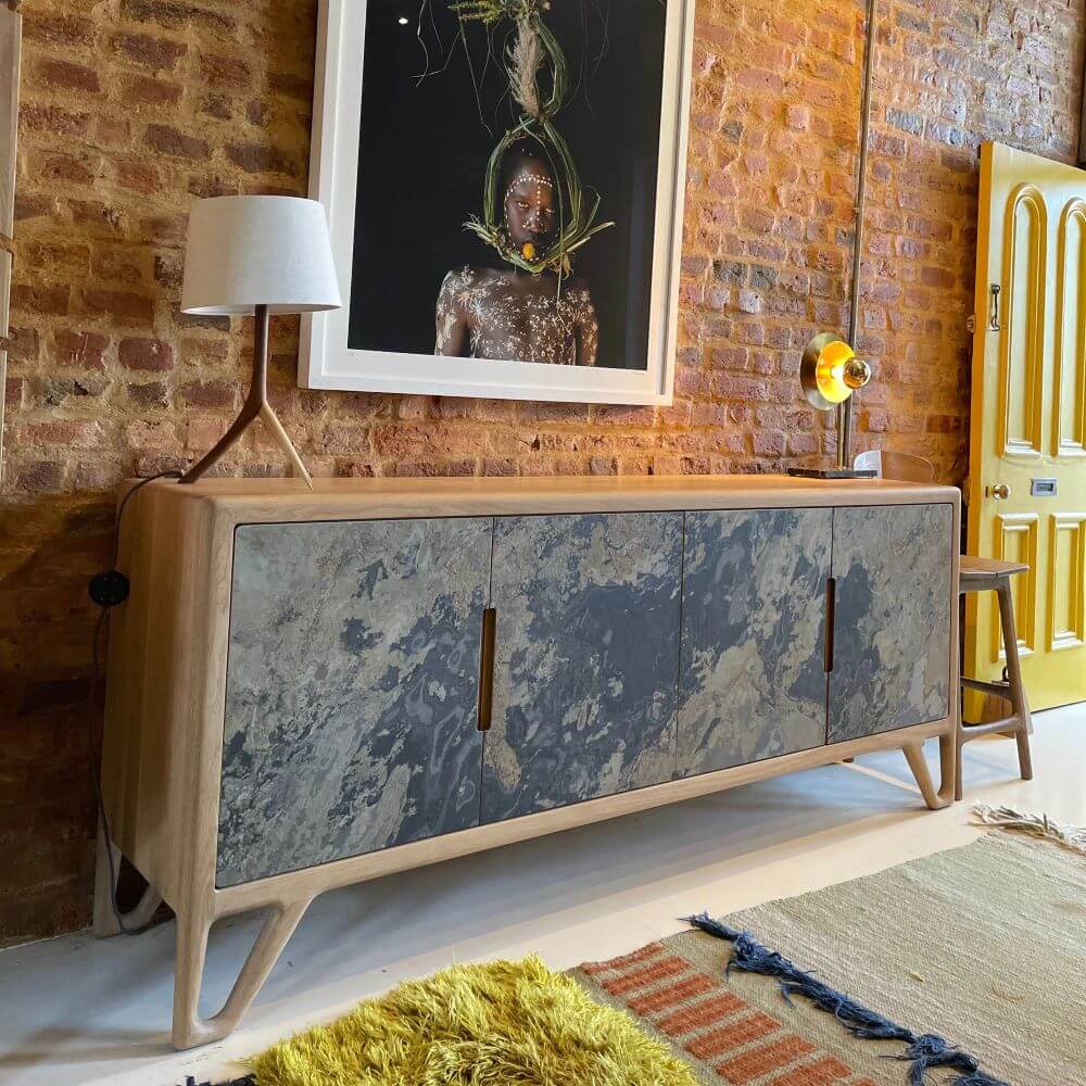 A grey-blue stone sideboard in front of a brick wall. The piece has 2 lamps on it.