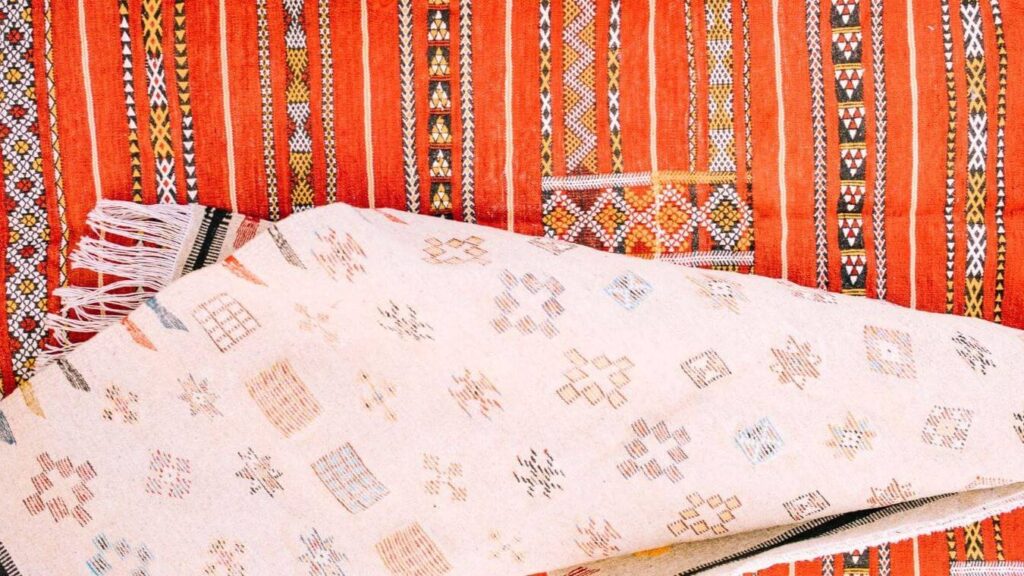 A white moroccan rug with colorful motifs layered over a vibrant orange moroccan rug