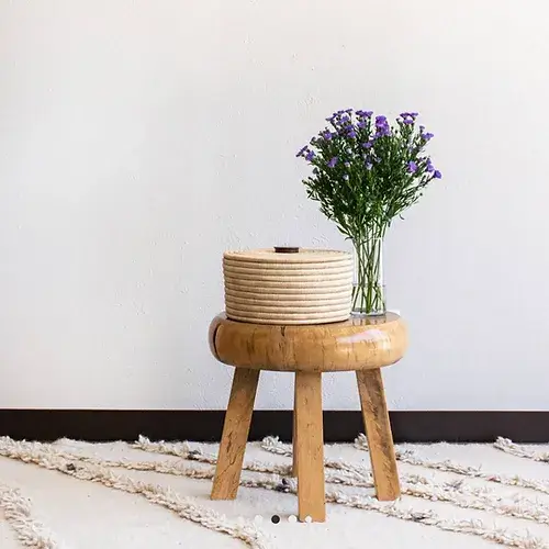 Small lidded woven basket in natural placed on a wooden stool next to a bouquet of purple flowers