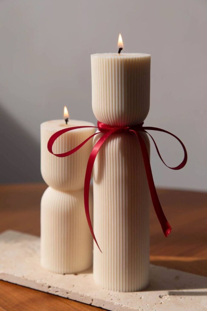 A tall and a small pillar-shaped candles in off-white, with a red ruban tied around the tall candles