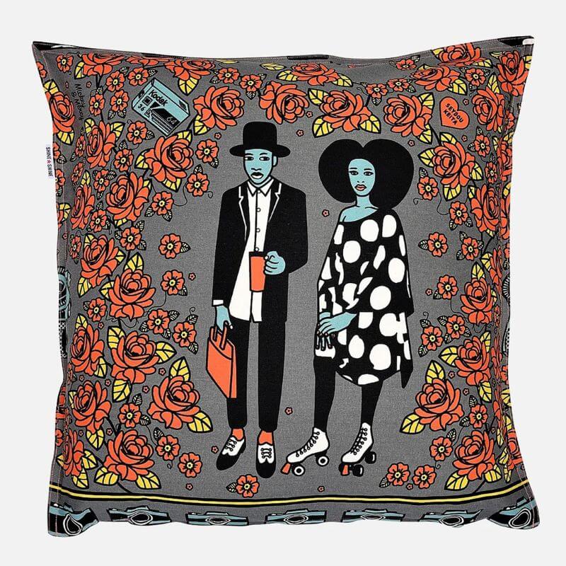 Gifts for Interior Design lovers - A gray-based cushion depicting the scene of a young African couple elegantly dressed in black and white white red roses all around them. The man is holding a coffee mug and a briefcase, the woman is wearing rollerblades. The bottom of the design is adorned by a row of cameras and a Kodak camera tape can be seen at the top-left