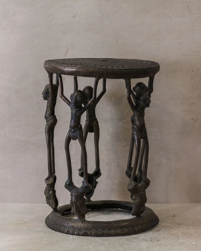 A bronze metal side table featuring ornate relief sculptures, depicting scenes from Benin's history, mythology, and royal court.