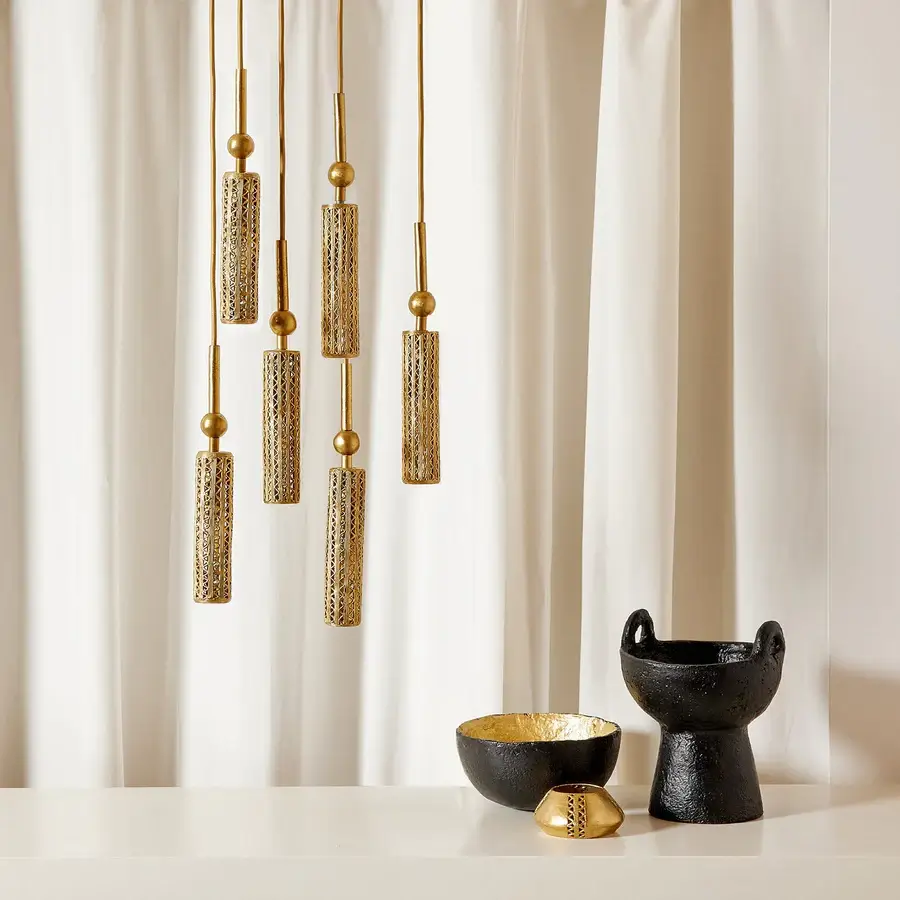 Golden brass chandelier made out of tubes of brass hanged to a golden wire. Black and gold decor items including a bowl and a vase