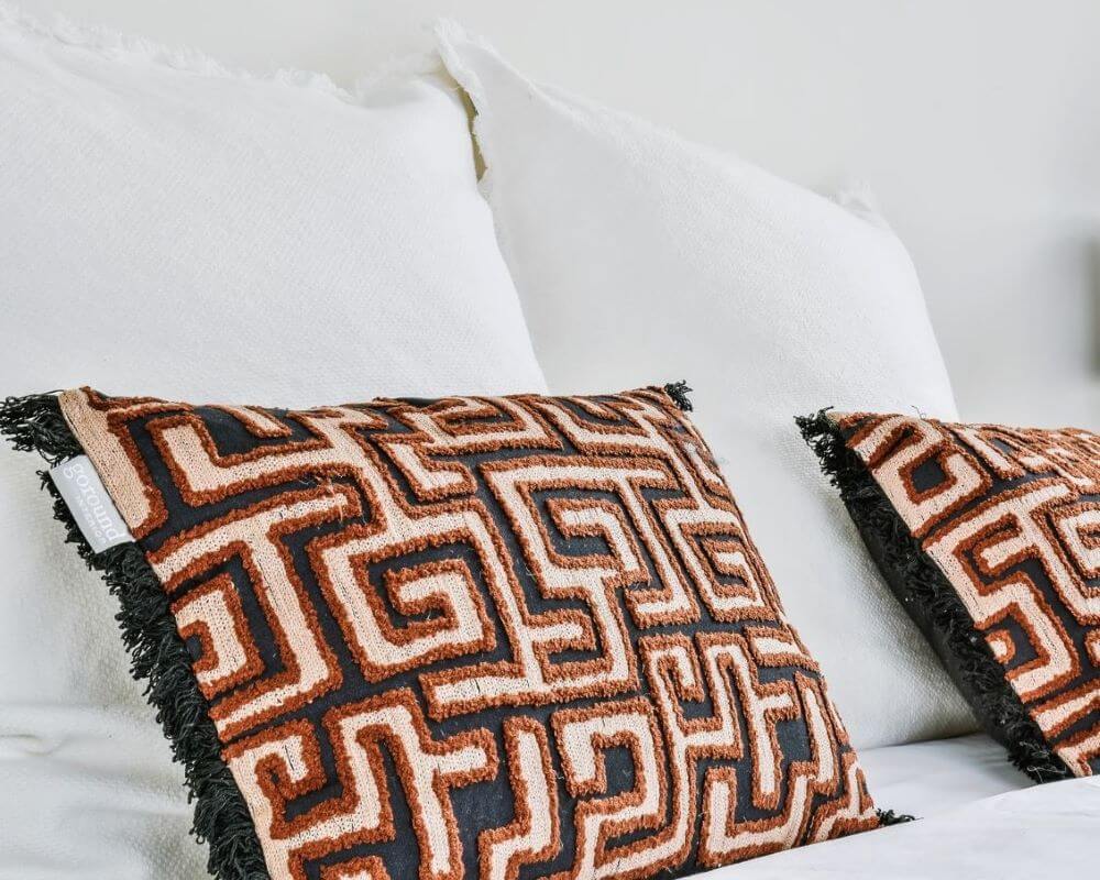 African bedroom decor - Throw pillows in black with Kuba cloth patterns in beige and terracotta, placed on a bed against white pillows