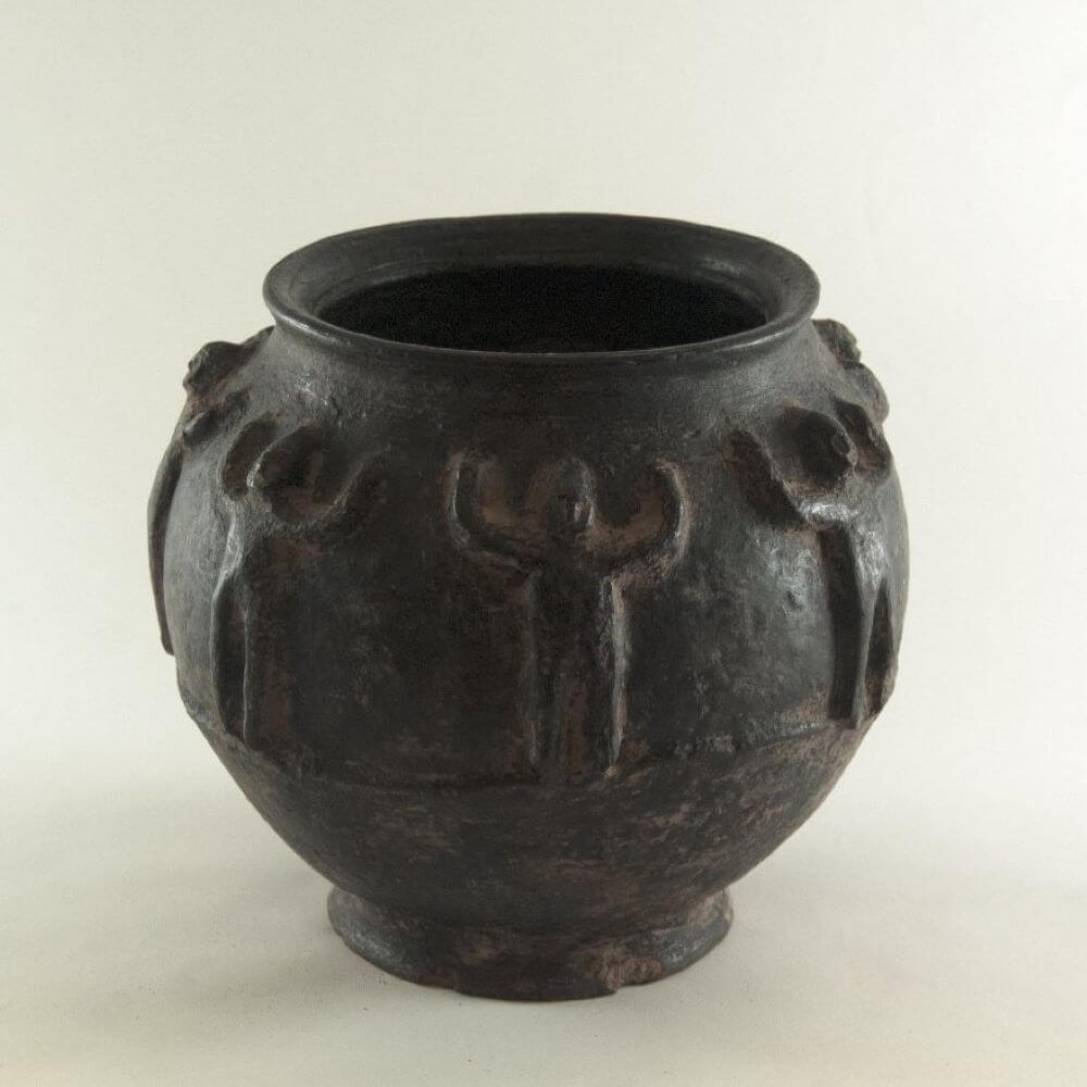 Black ancient pot from the Bamana people of Mali with a circular design and seven standing figure molded on the surface