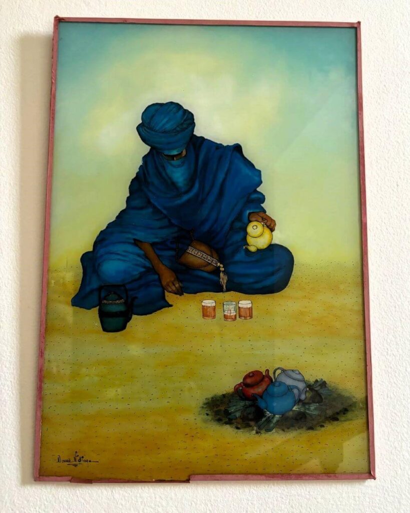 Glass painting of a desert nomad bedouin in an alluring blue outfit, seated in lotus pose. He is making and pouring mint tea in small glasses.