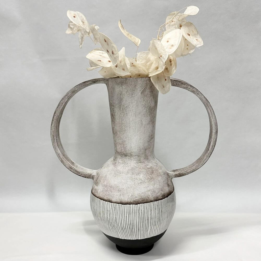 Ceramic vase with two semi_circle arms in grey, with a white striped base and a black bottom. White flowers in the vase.