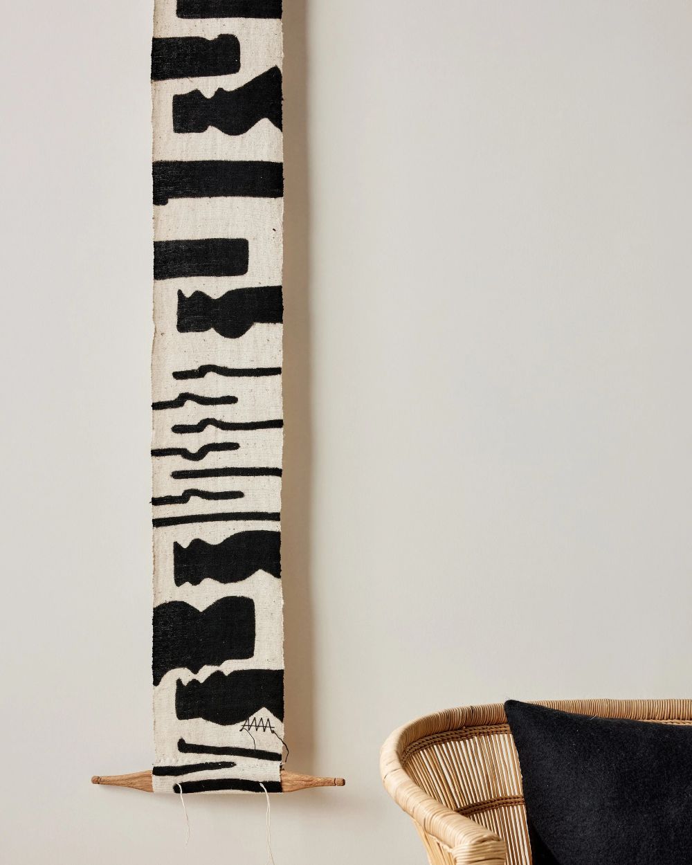Wall art totem made out a wide strip of fabric with a white background and black patterns painted with the Bogolan technique