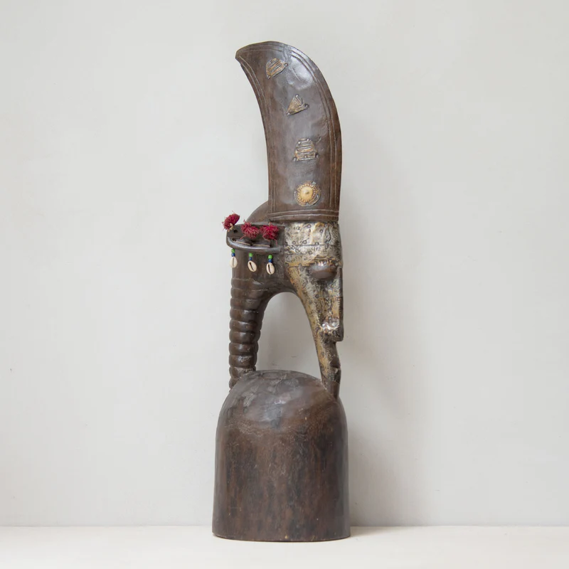 Niger Helmet mask in wood with brass accents with a unique shape. A few decorative cowries and pink synthetic flowers adorn it.