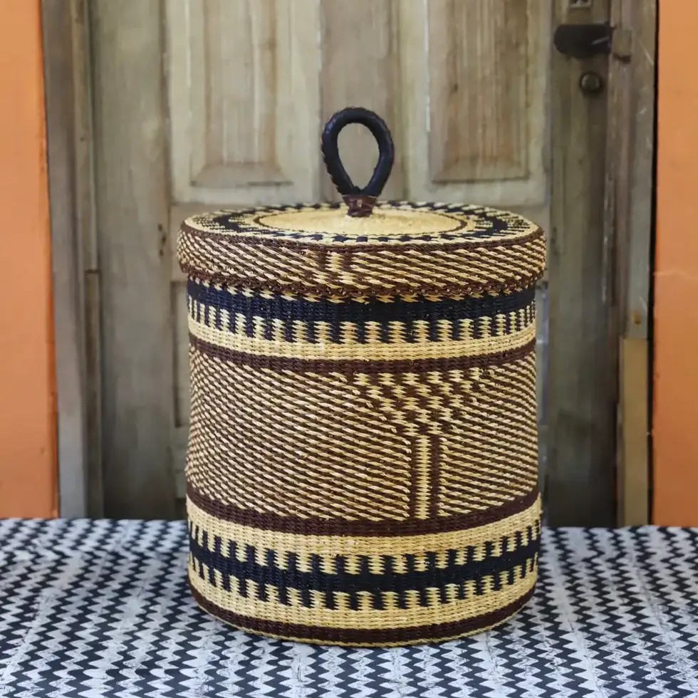 Woven laundry basket with a lid. It has a natural color accented with elegant navy and brown patterns