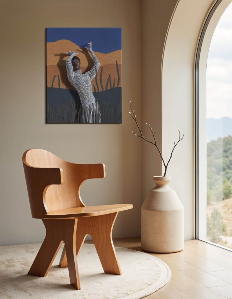 A stylish, light-wood, modern art chair sits on a cream-colored rug, next to a tall off-white vase holding a small budding branch, near an arched window with a mountain view. On the wall behind hangs a Modern African art painting showing a man in an abstract landscape. The chair is a striking, blending form and function.