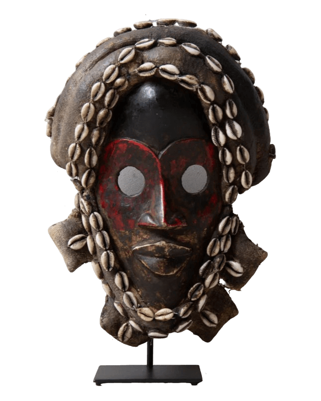 A vibrant artistic mask, resting on a sleek black stand. The mask displays an abstract face design with red accents and striking cowrie shell embellishments.