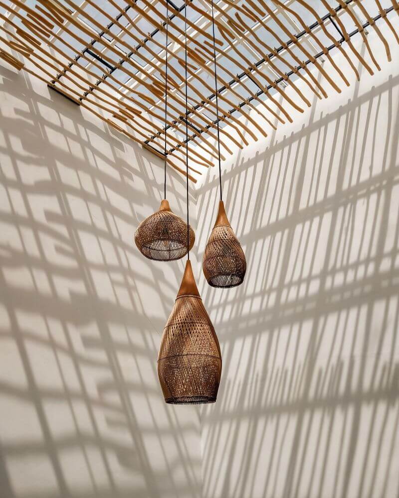 Three stylish woven pendant lights hang beneath a unique ceiling design, casting patterned shadows. Perfect lighting to enhance the ambiance of any room.