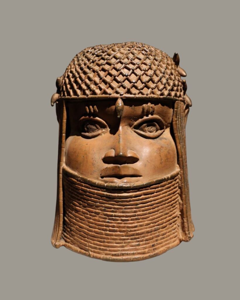 A bronze head sculpture, likely West African, with a serene facial expression under an intricate crown.