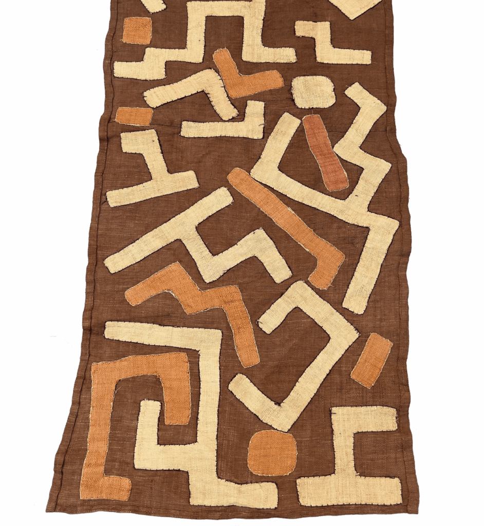 Close-up of vintage Kuba cloth featuring geometric patterns in beige and orange against a brown backdrop.