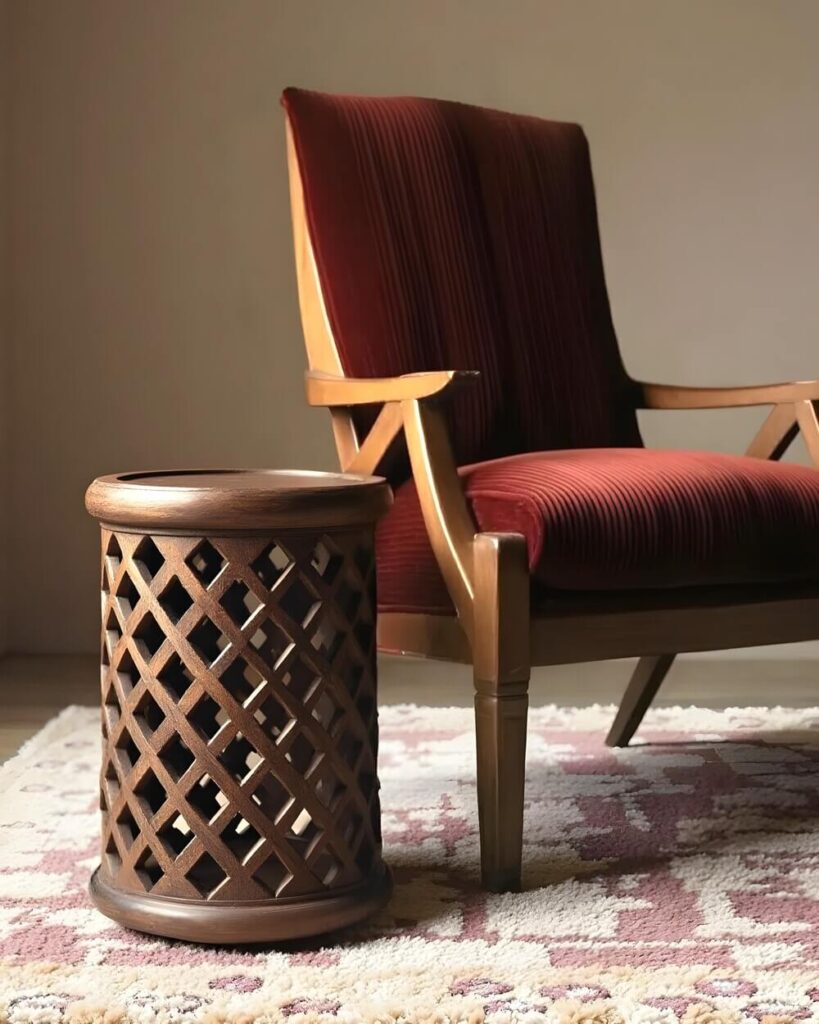 Living room showpiece: A wooden side table in the Bamileke table style with a diamond cutout design stands next to a red velvet chair on an off-white rug with a pink floral pattern.