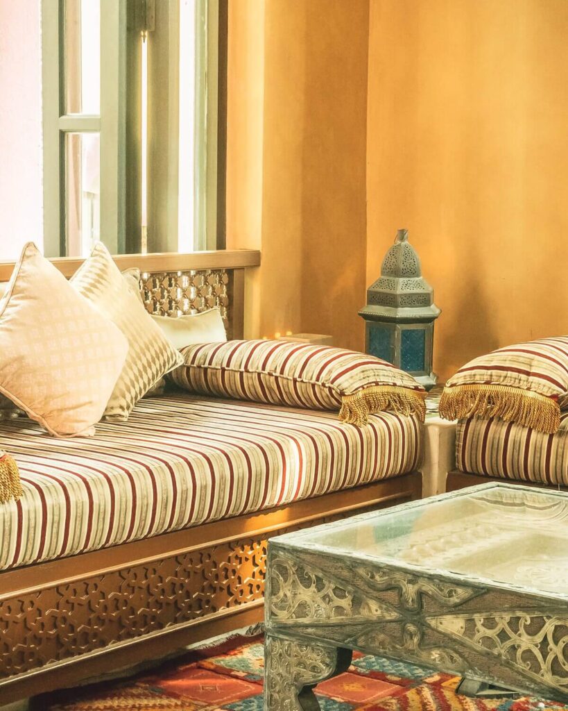 Moroccan interior design featuring a cozy nook with striped cushions, ornate wooden furniture, and a decorative metal lantern.