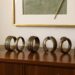 A row of ornate, African bronze bangles with intricate patterns displayed on a wooden cabinet under a framed abstract art piece in a modern, elegant room.