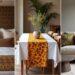A collage of three cozy interior settings with African print textiles used as decor. Left: A bed with white and brown patterned bedding and pillows. Center: A dining table with an orange floral runner and a vase of greenery. Right: A beige sofa with colorful cushions next to a floor lamp.
