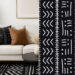 A wide image separated in two parts. The left part show a modern living room with an off white couch, a black mud cloth throw pillow, a brow throw pillow, a black and white mud cloth rug, a plant, a vase and an artwork. The right part is a close up on black and white African mud cloth patterns.