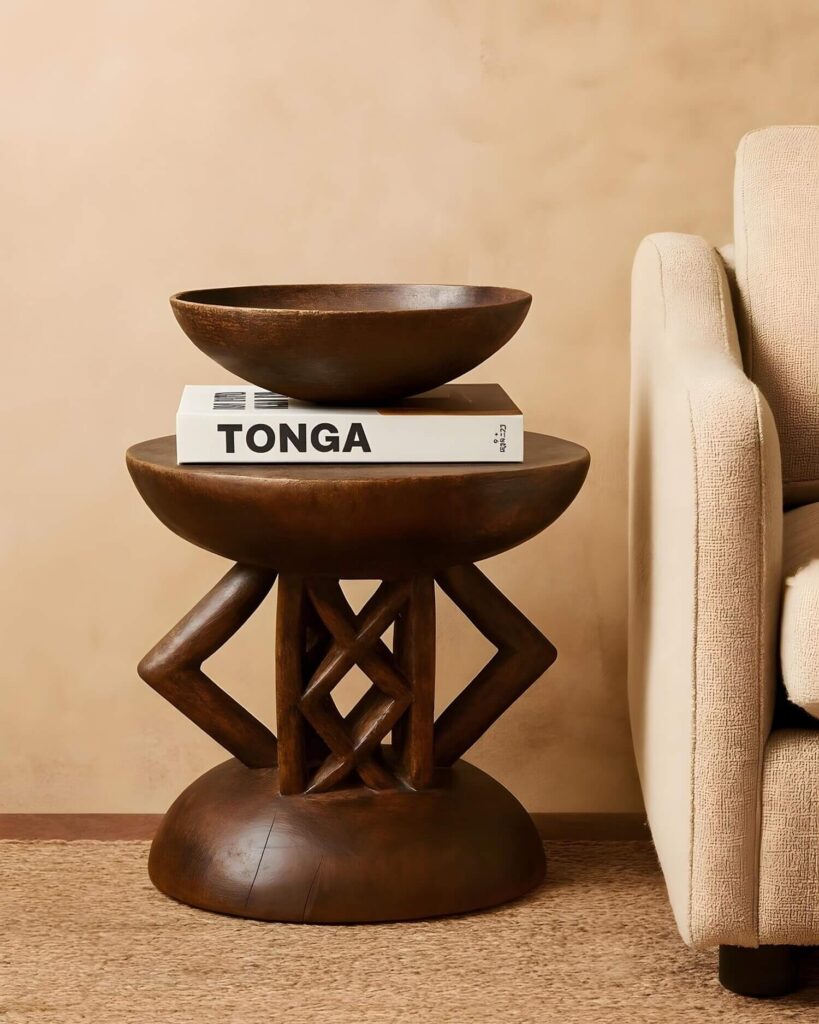 Gorgeous Tonga stool with geometric carvings used as a decorative side table with a chic coffee table book and a vintage African bowl stacked on it.
