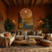 Warm-toned African-style home with elegant decor. Beige sofas, earthy cushions, large abstract painting, wooden coffee table, and lush plants create a cozy ambiance. A dining room can be seen in the back on the left, and a terrace sits behind a tall glass window on the right.
