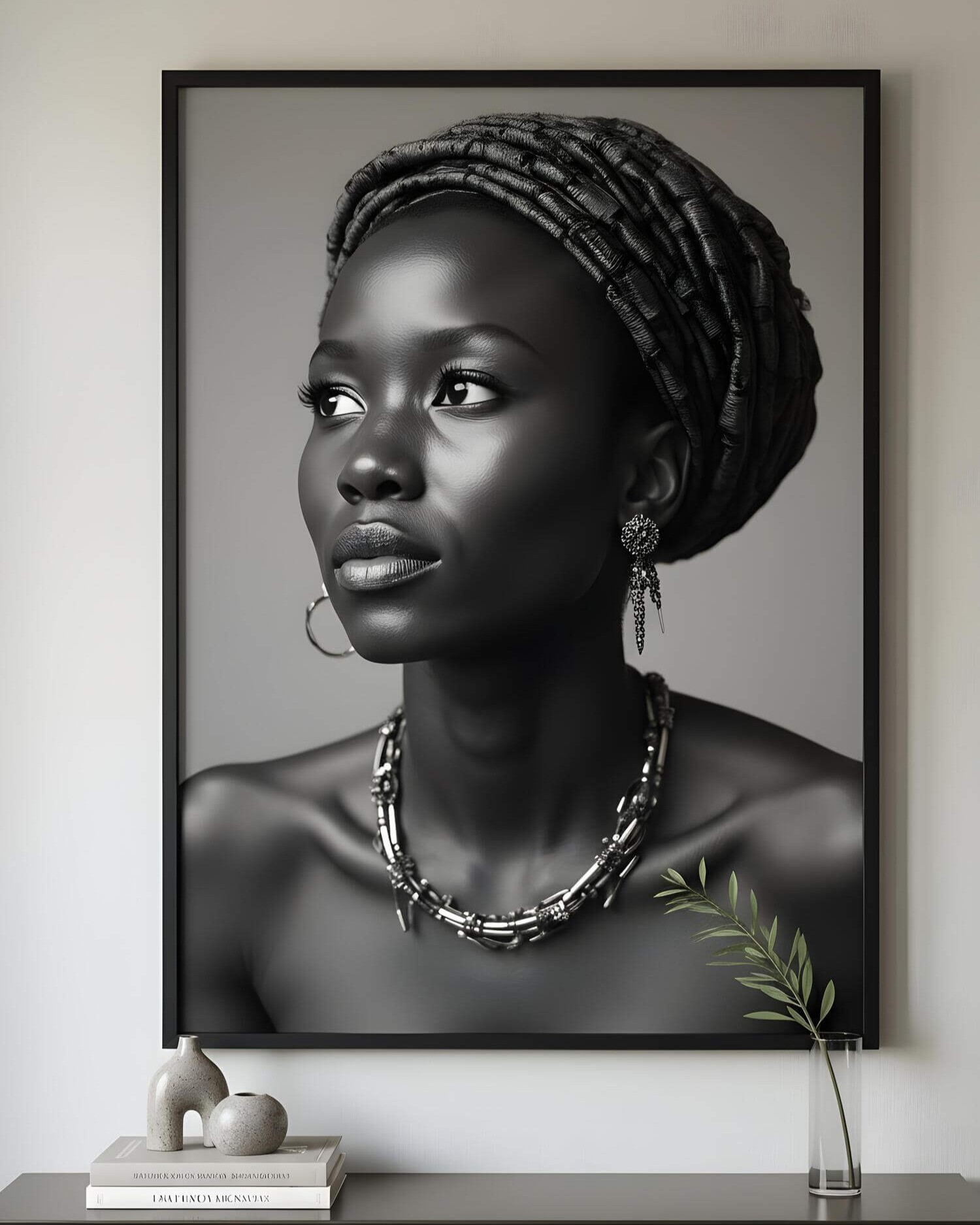 Black and white portrait of a woman in a textured headwrap and jewelry. She gazes upward with a serene expression. Framed on a minimalist wall.