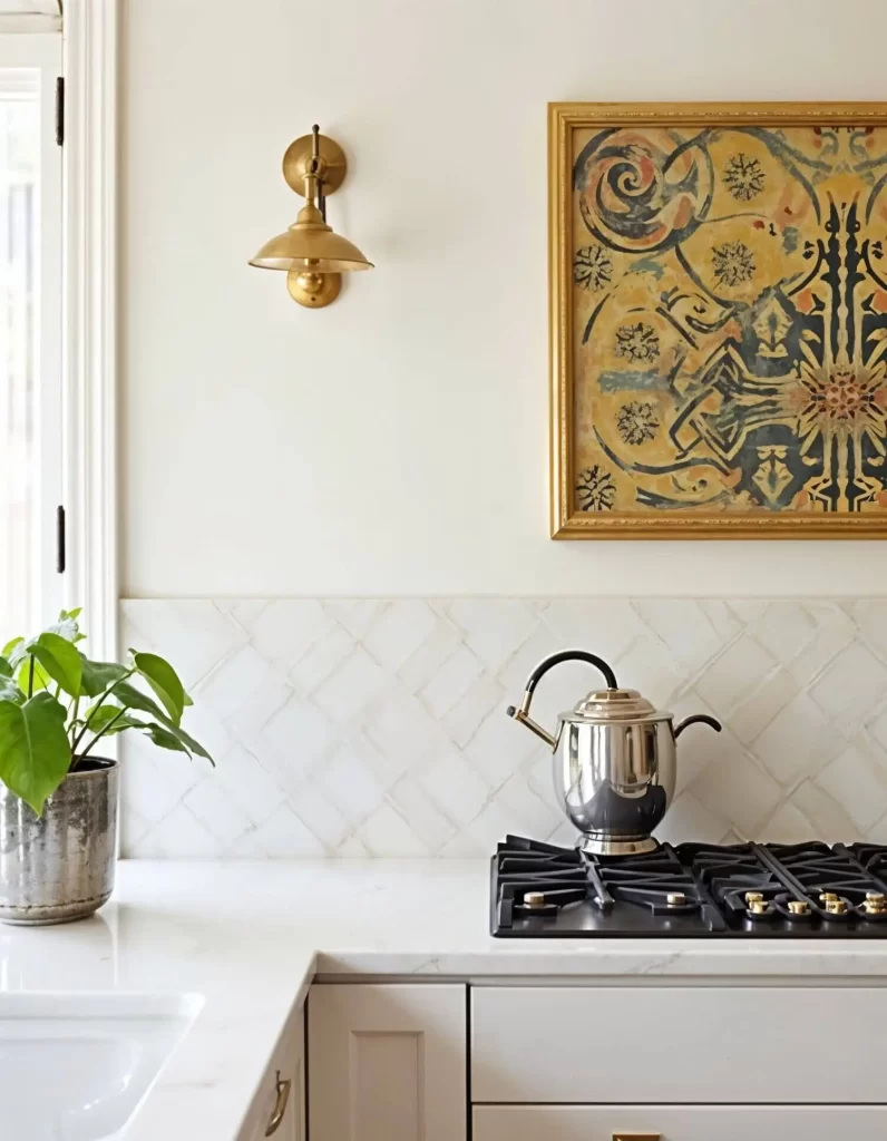 A close-up of a stove and white countertop with a quilted white tile backsplash. A single brass wall-mounted task sconce with a classic shade is positioned above the backsplash, next to a framed piece of art.