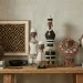 A gorgeous display of African artifacts: left to right: a Zulu pot placed on a stack of books, framed kuba cloth on the wall, an Ethiopian Gurage bowl, 3 namji dolls at the center, a Maasai bead collar on a wood bust and a Punu mask on a stand