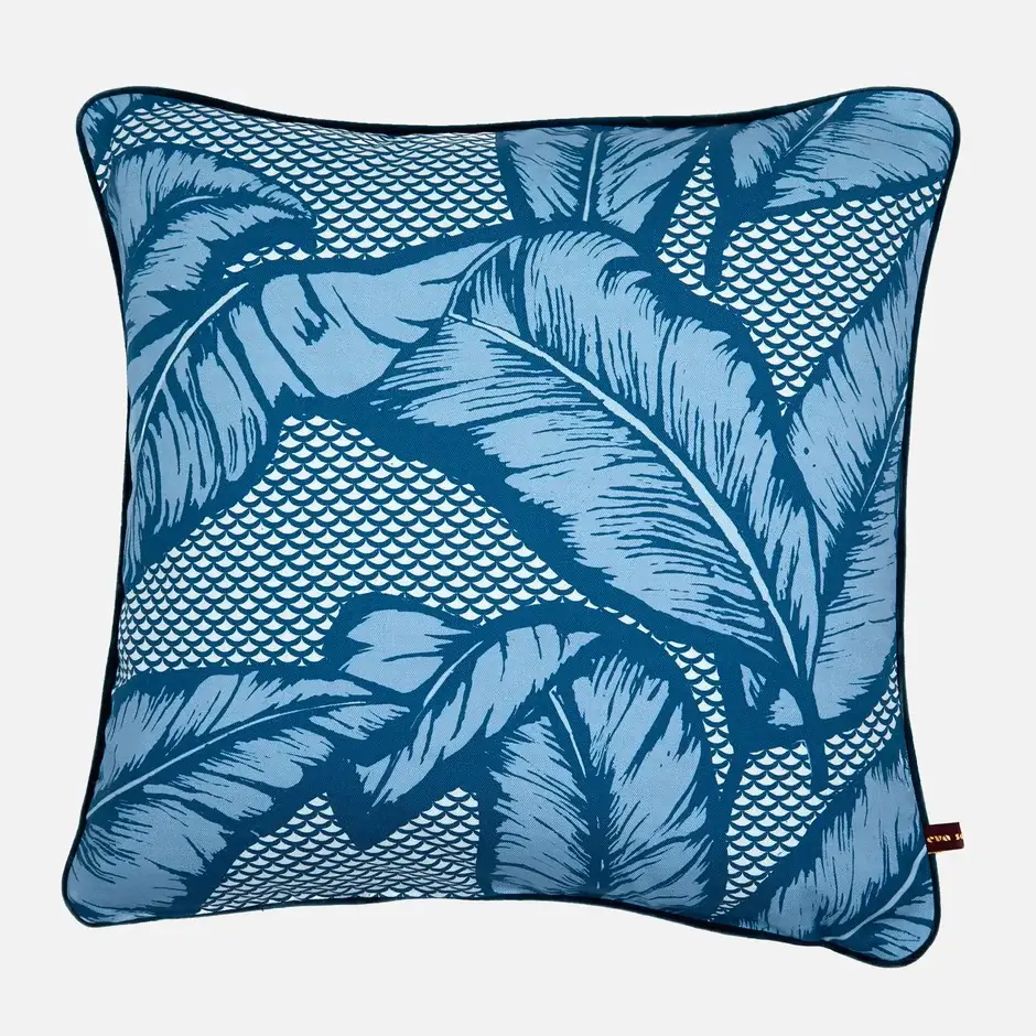 A blue throw pillow with large tropical leaf prints on it