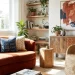 Sunlit living room with a rust-colored sofa, woven accent chair, abstract wall art, and natural wood furniture showcasing earthy textures and 2026 interior design trends.