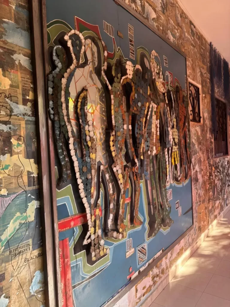 An angled perspective of the same mixed-media silhouette artwork, highlighting the three-dimensional depth of the textured materials and the surrounding wall, which is covered in a collage of newsprint and torn paper.
